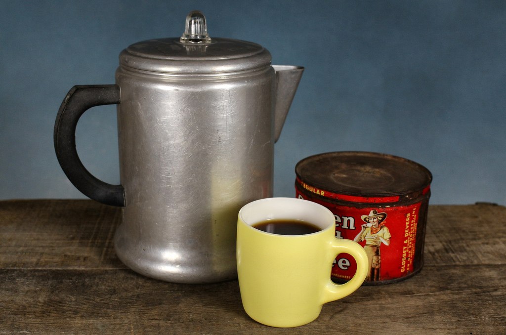 Old percolator with ground coffee and mug.